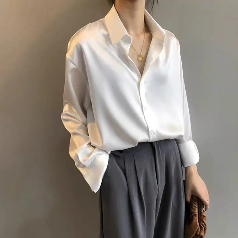 Une femme portant une blouse blanche en satin avec un col classique, associée à un pantalon gris à plis, créant une tenue élégante et sophistiquée, parfaite pour un look raffiné.