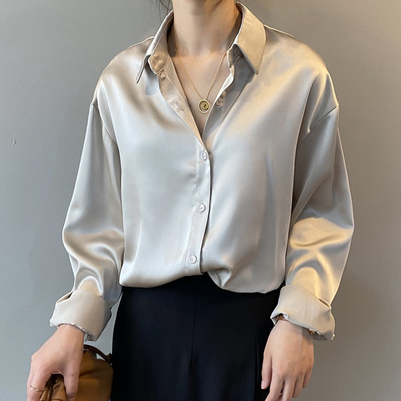 Une femme portant une blouse satinée beige avec un col classique, associée à un pantalon noir, créant une allure élégante et raffinée, parfaite pour un look chic et intemporel.