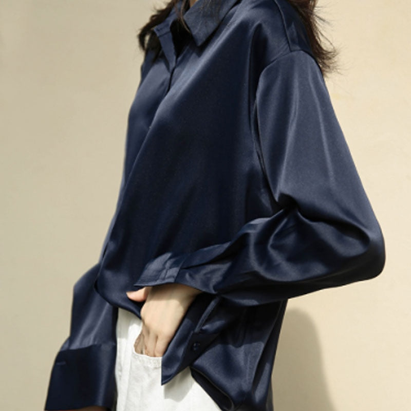 Une blouse en satin bleu marine avec des manches longues légèrement retroussées et un col classique, portée avec une silhouette élégante et décontractée.