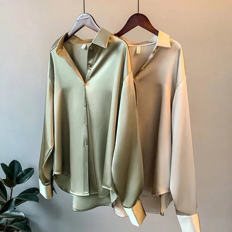 Deux blouses élégantes suspendues à des cintres, l'une de couleur beige et l'autre de vert olive, avec un col classique et des manches longues, parfaites pour un look raffiné et intemporel.
