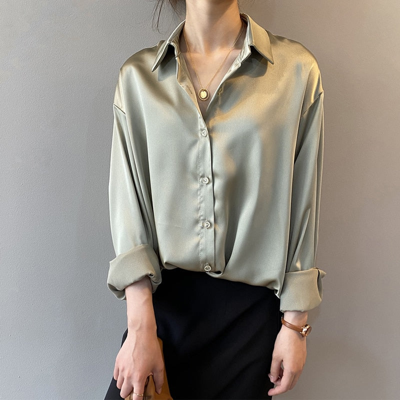 Une femme portant une blouse satinée de couleur vert clair avec un col classique, associée à un pantalon noir, créant un look élégant et intemporel, parfait pour un style raffiné.
