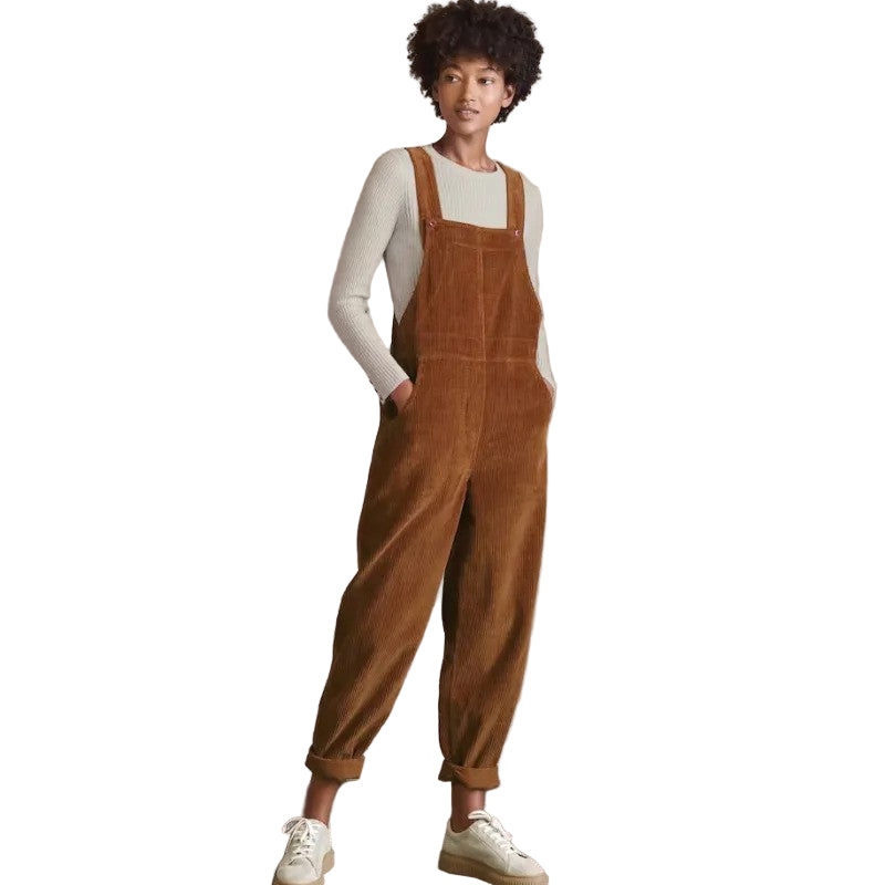 Femme portant une salopette en velours côtelé marron avec un pull beige à manches longues, associée à des baskets blanches, dans une pose décontractée.