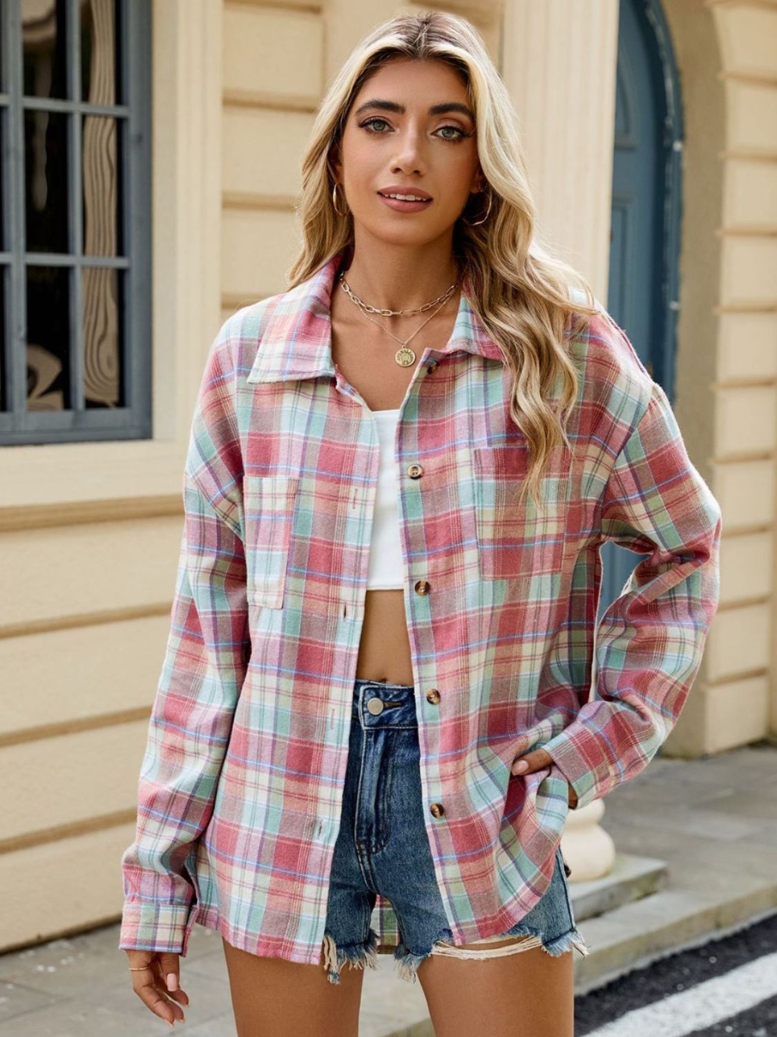 Femme portant une chemise longue à carreaux aux tons pastel, avec un crop top blanc et un short en jean, adoptant un style décontracté et moderne en extérieur.