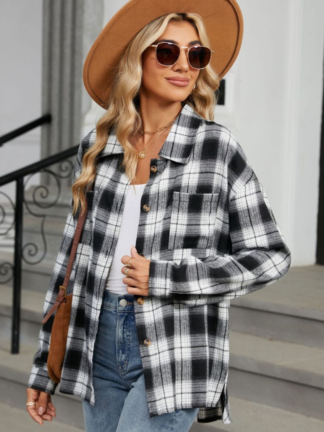 Femme portant une chemise longue à carreaux noir et blanc, un t-shirt blanc, un jean et un chapeau beige, complétant son look moderne avec des lunettes de soleil et un sac en bandoulière.