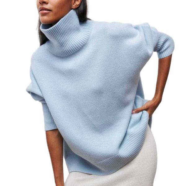 Femme portant un pull à col roulé ample de couleur bleu clair, confectionné dans une maille douce et épaisse. Le vêtement présente une coupe oversize avec des bords côtelés au col, aux manches et à la base. Ce pull dégage une allure confortable et élégante, idéal pour la saison hivernale ou les journées fraîches, combiné ici avec une jupe claire pour un style moderne et minimaliste.
