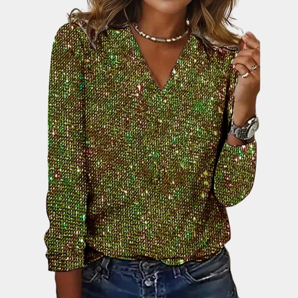 Top à manches longues orné de sequins verts et dorés, avec un décolleté en V. Le modèle est accompagné d’un jean décontracté et de bijoux minimalistes, créant un look scintillant et élégant.