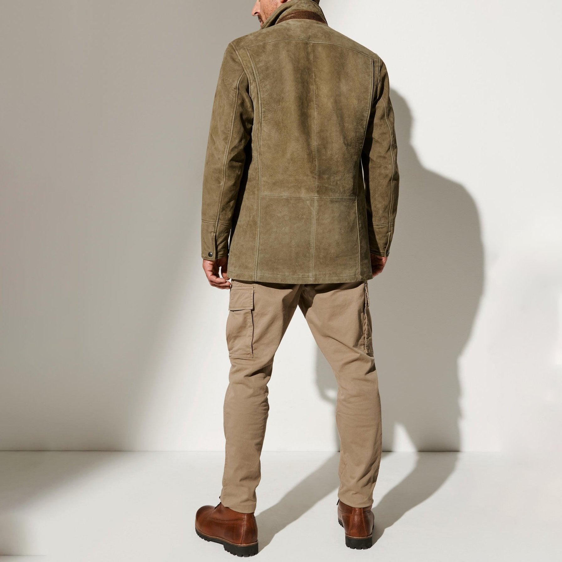 Vue arrière d'un homme portant une veste en cuir vintage avec des détails en cuir contrasté, associée à un pantalon beige et des chaussures robustes. L'ensemble présente un look classique et raffiné, idéal pour un style élégant et intemporel.