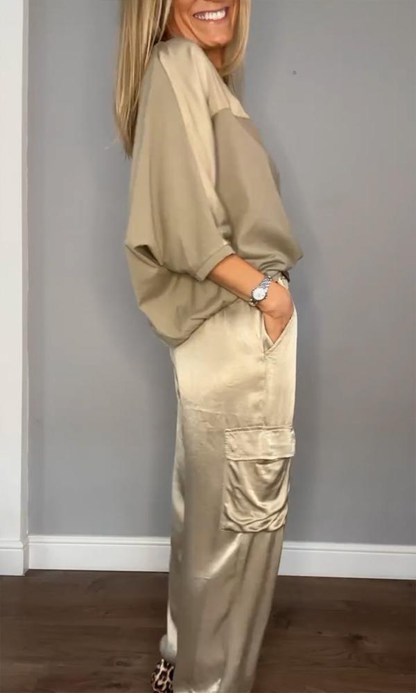 Un ensemble chic composé d'un haut beige fluide avec des manches tombantes et d'un pantalon satiné de couleur crème avec des poches. La tenue est accompagnée de talons à motif léopard.