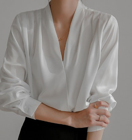 Blouse élégante à manches bouffantes et décolleté en V, portée par une femme avec un pantalon noir et des bijoux délicats.