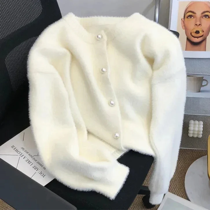 Cardigan en tricot doux de couleur blanche avec des boutons en perle. Ce modèle est posé sur une chaise, mettant en avant sa texture et ses détails élégants.