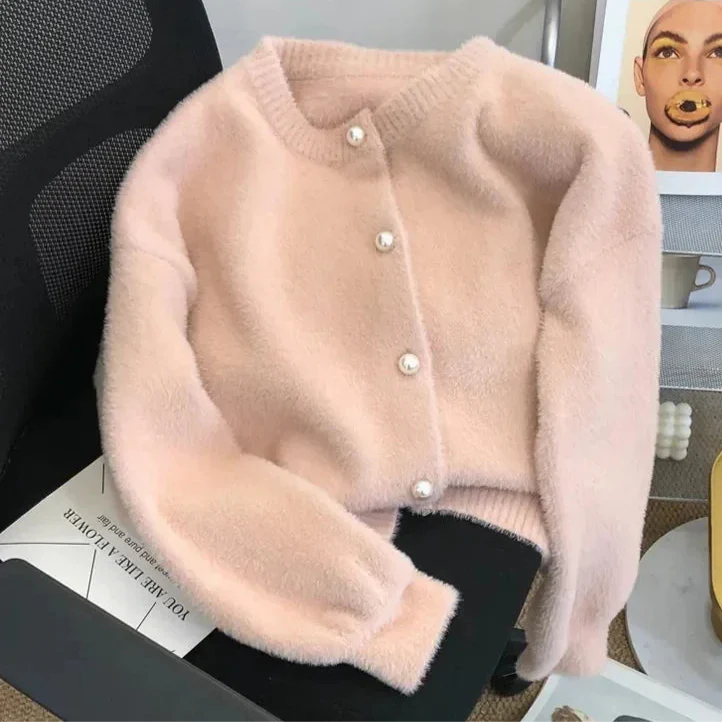 Cardigan en tricot doux de couleur rose pâle avec des boutons en perle. Il est posé sur une chaise, mettant en avant sa texture duveteuse et son style élégant.