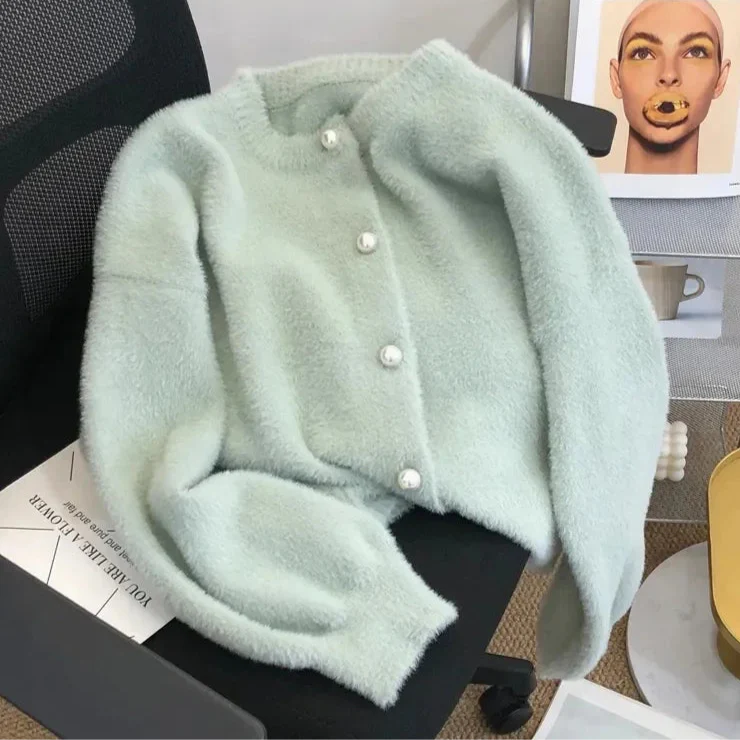 Cardigan en tricot doux de couleur bleu pâle avec des boutons en perle, posé sur une chaise. Le tissu duveteux et la texture délicate du cardigan ressortent sur le fond minimaliste.