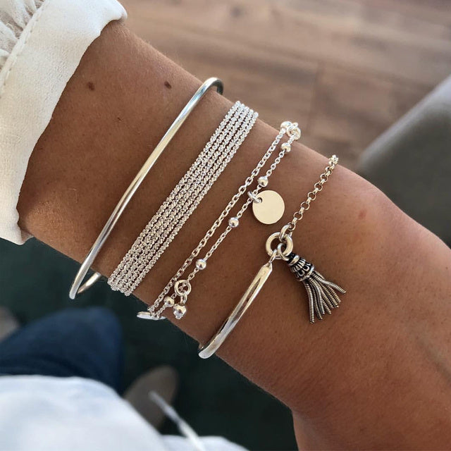 Un ensemble de bracelets fins en argent, avec un design boho charmant. L'ensemble comprend des bracelets avec des détails en perles, un pendentif rond et un pendentif en forme de franges, parfaits pour un style bohème élégant.