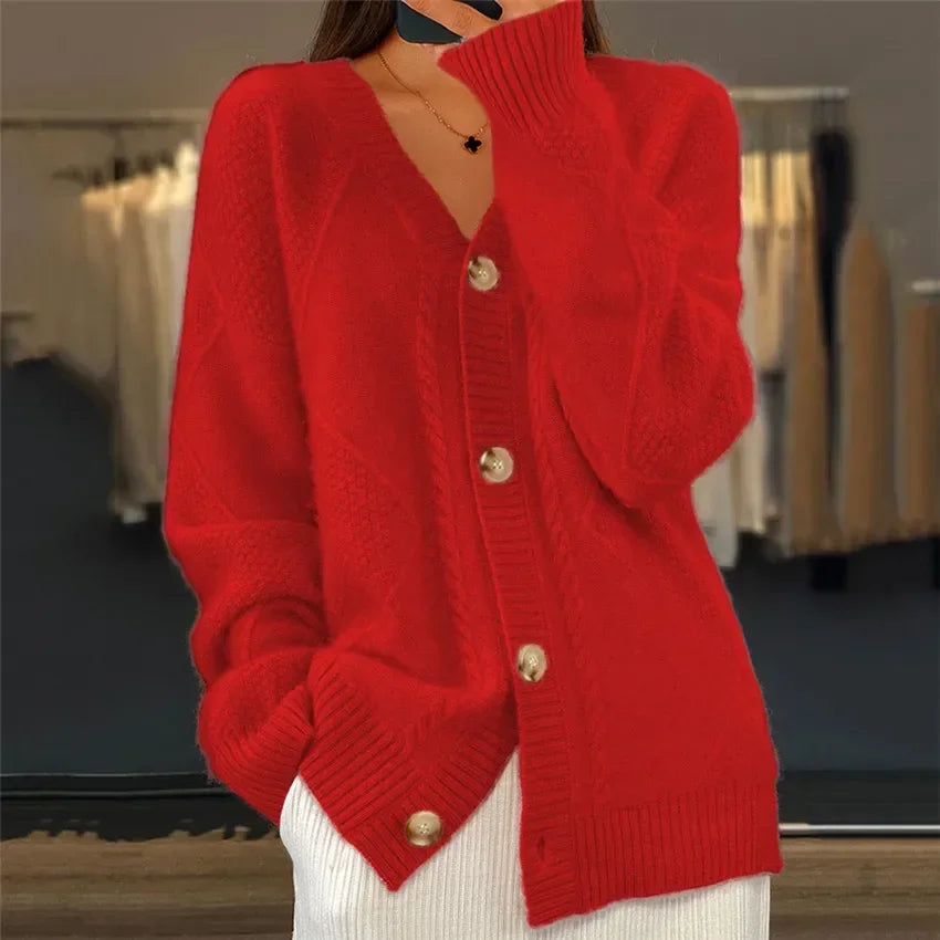 Femme portant un cardigan rouge vif en tricot avec un col en V, des boutons en bois et un motif torsadé. Elle tient une main près du visage tout en ayant une apparence élégante.