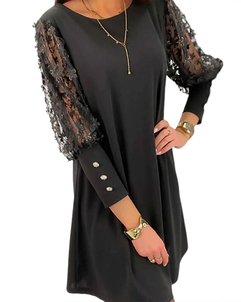 Femme portant une robe noire fluide à manches trois-quarts ornées de dentelle transparente décorée de fleurs brodées. Les manches sont embellies de boutons scintillants ajoutant une touche raffinée. La coupe droite de la robe crée une allure chic et confortable, parfaite pour une fête ou une soirée élégante. L’ensemble est complété par des bijoux dorés qui accentuent l’élégance du look.