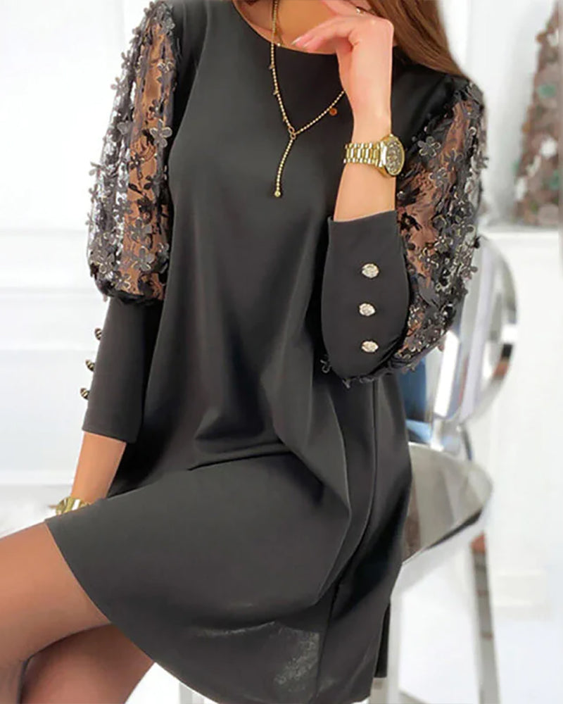 Femme portant une robe noire élégante à manches trois-quarts ornées de dentelle transparente et de broderies florales. Le tissu fluide tombe légèrement au-dessus des genoux, créant une silhouette raffinée. Les manches sont décorées de boutons brillants, ajoutant une touche sophistiquée. La tenue est accessoirisée avec des bijoux dorés, idéale pour une soirée ou un événement festif.