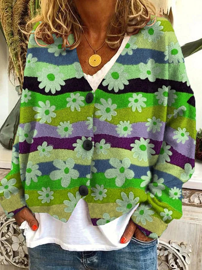 Femme portant un cardigan à boutons orné de rayures ondulées vertes, violettes, bleues et jaunes, décoré de fleurs blanches. Le vêtement a une coupe décontractée et est assorti à un t-shirt blanc et un jean bleu. Le style évoque une allure vintage et bohème, parfaite pour un look coloré et original.