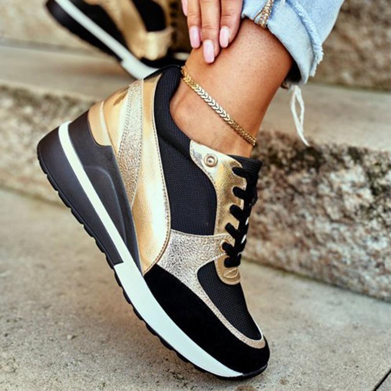 Une paire de baskets féminines au design moderne, combinant le noir et l’or métallique. Les chaussures présentent une semelle blanche épaisse et un mélange de matières en cuir et tissu pour un style chic et sportif. Le modèle est porté avec un jean retroussé, mettant en valeur une chaîne de cheville dorée, pour une allure urbaine élégante et tendance.