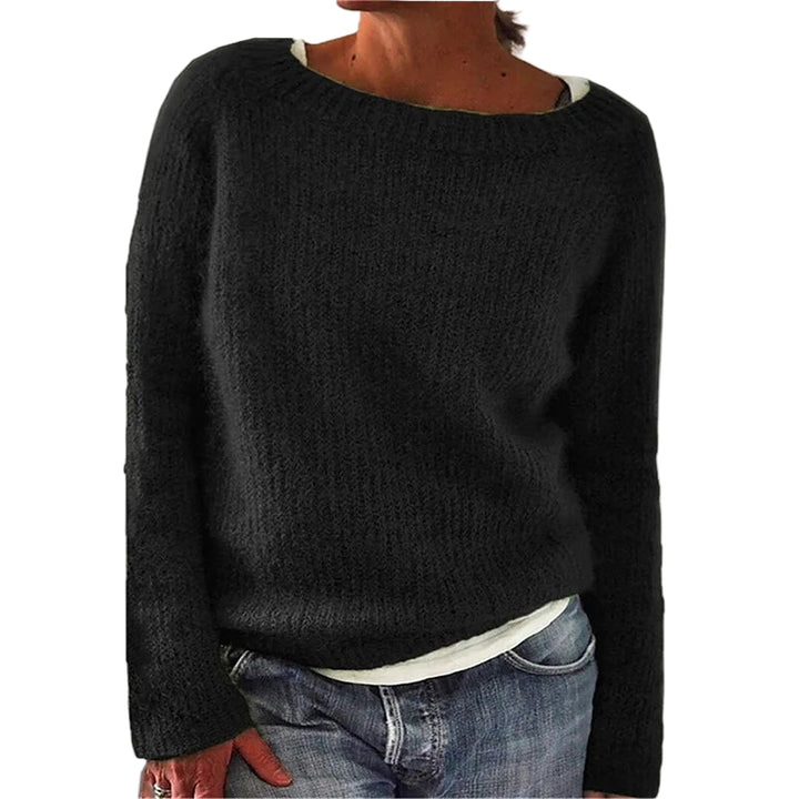 Femme portant un pull en maille noir à manches longues, à coupe décontractée et encolure large, associé à un t-shirt clair et un jean, photographiée devant un fond neutre.