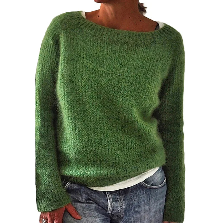 Femme portant un pull en maille vert à manches longues, à coupe décontractée et encolure large, associé à un t-shirt clair et un jean, photographiée sur un fond blanc.