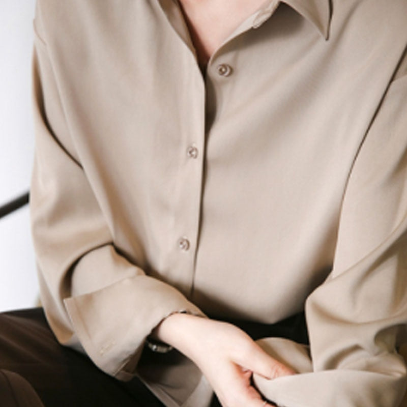 Détail d'une blouse beige avec un col classique et des manches longues légèrement retroussées, offrant un look élégant et décontracté, parfait pour un style raffiné.
