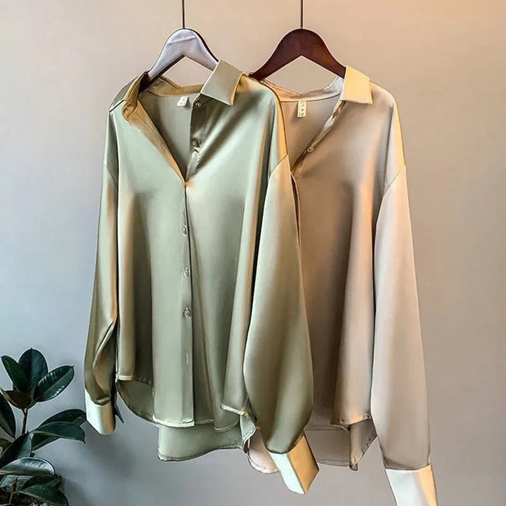 Deux blouses élégantes suspendues à des cintres, l'une de couleur beige et l'autre de vert olive, avec un col classique et des manches longues, parfaites pour un look raffiné et intemporel.