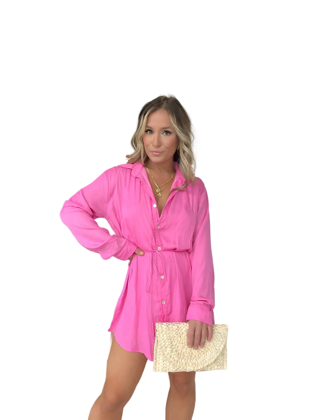 Chemise à manches longues pour femme, modèle tendance. Cette chemise fluide de couleur rose vif, avec des boutons et une ceinture à nouer à la taille, crée une silhouette élégante et décontractée. Elle est portée avec un sac en osier et des accessoires dorés, parfaits pour un look chic et moderne.