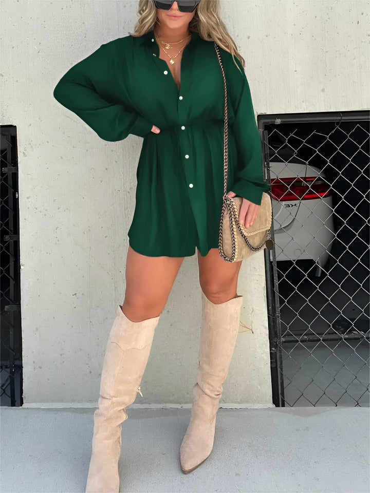 Chemise à manches longues pour femme, modèle tendance. Cette chemise fluide de couleur vert émeraude, avec des boutons et une ceinture à nouer à la taille, crée une silhouette élégante et décontractée. Elle est portée avec des bottes hautes beiges et un sac à bandoulière, parfait pour un look moderne et chic.