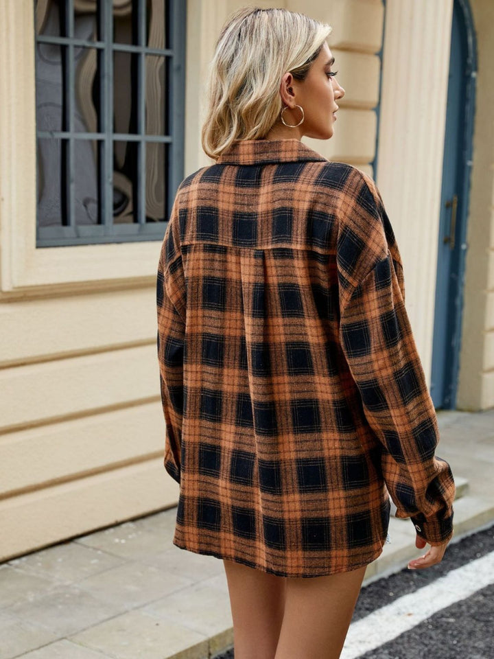 Vue arrière d'une femme portant une chemise longue à carreaux orange et noir, avec des manches longues, des boucles d'oreilles dorées, et un regard tourné vers la droite dans un cadre urbain.