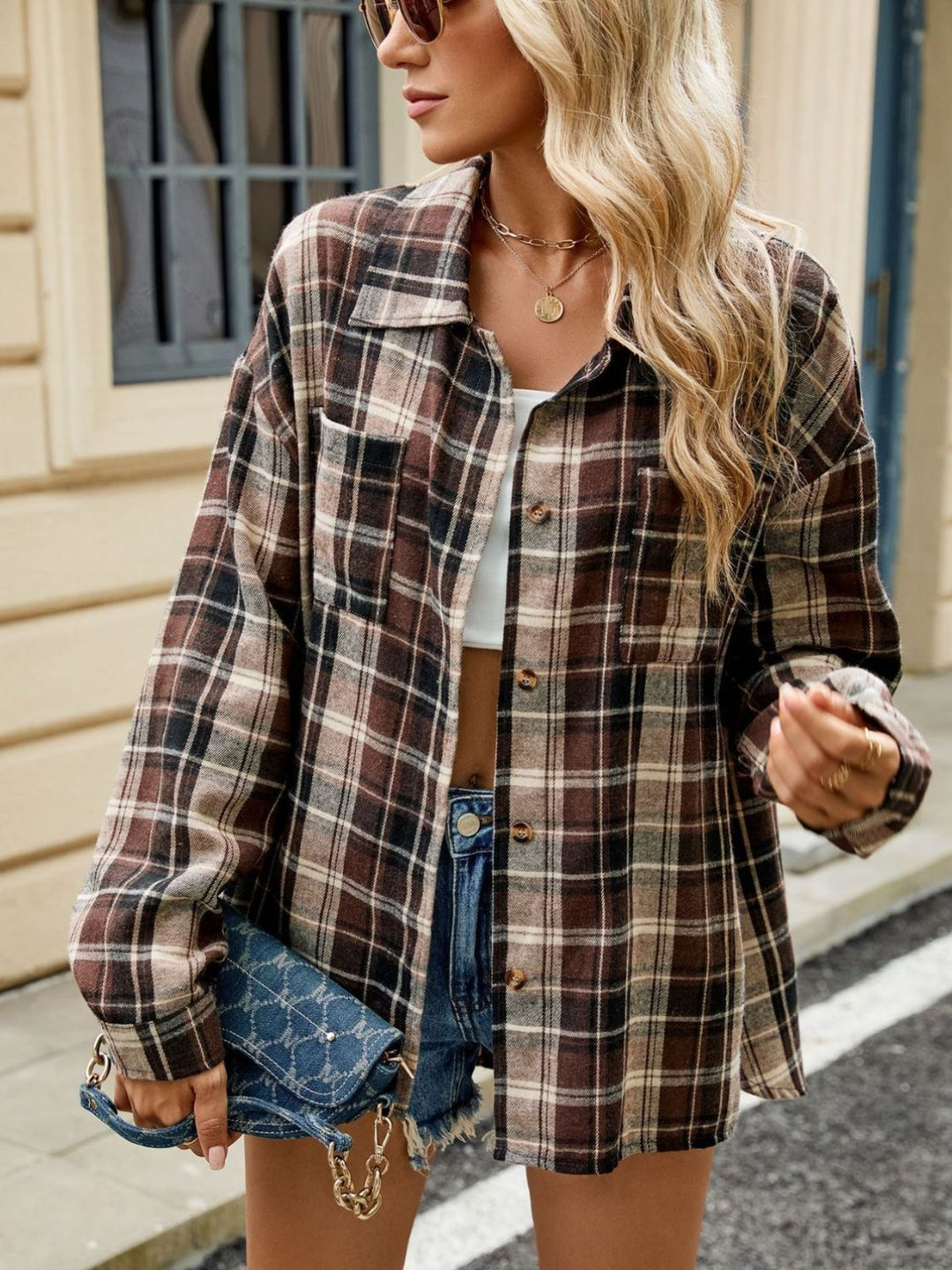 Femme portant une chemise longue à carreaux marron et crème avec des boutons, une coupe décontractée, un top blanc, des lunettes de soleil et un sac à main en chaîne, posant dans une rue urbaine.