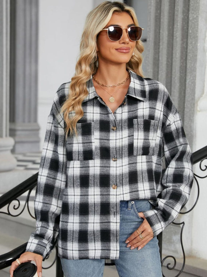 Femme portant une chemise à carreaux noir et blanc avec des boutons, des lunettes de soleil et un pantalon en jean, souriant dans une ambiance urbaine.