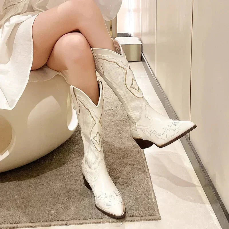 Des bottes blanches de style cowboy, à la coupe moderne et élégante, avec des motifs brodés délicats sur toute la tige. Ces chaussures s'arrêtent juste en dessous du genou et sont accompagnées d'un talon bloc discret. Elles apportent une touche sophistiquée et audacieuse à n'importe quelle tenue, parfaites pour un look tendance et affirmé.