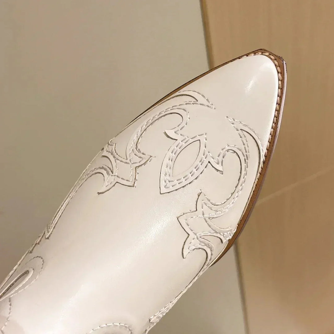 Zoom sur le bout pointu d'une botte blanche, mettant en valeur les motifs brodés fins et détaillés. La couture apparente et le cuir lisse créent une texture élégante et raffinée, accentuée par la finition soignée du bout.