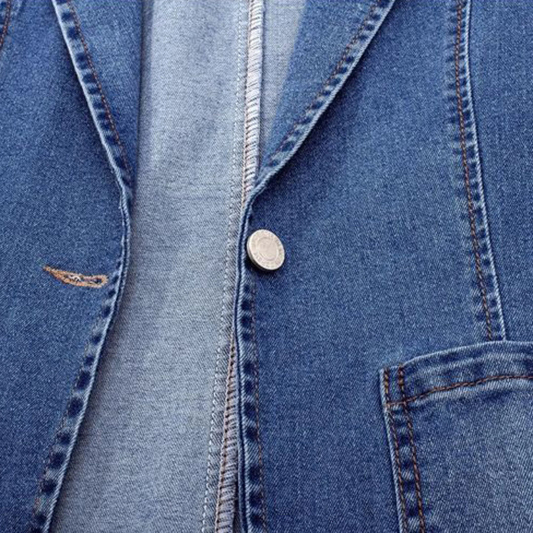 Détail du bouton et de la couture du blazer en denim bleu. Ce design soigné met en valeur l'aspect élégant et moderne du vêtement, avec une touche de finition raffinée.