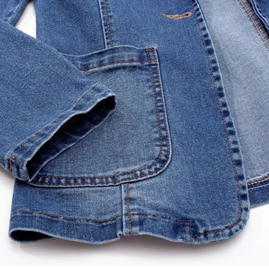 Détail de la poche et de la manche du blazer en denim bleu. Ce design met en avant la finition soignée et la coupe contemporaine, parfaite pour un look chic et décontracté.