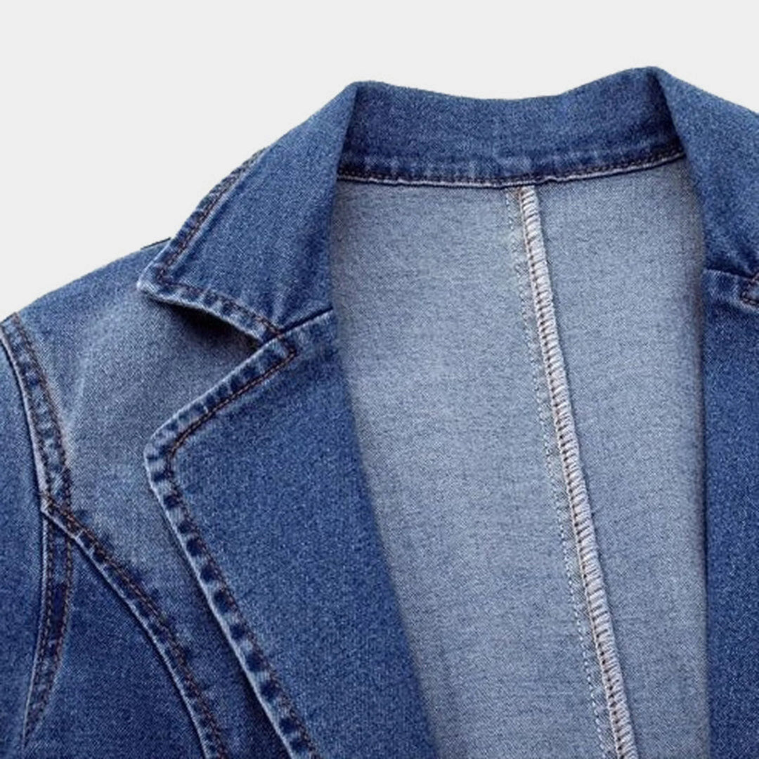 Détail du col et de la couture du blazer en denim bleu, soulignant sa coupe soignée et son design moderne, parfait pour une tenue à la fois chic et décontractée.