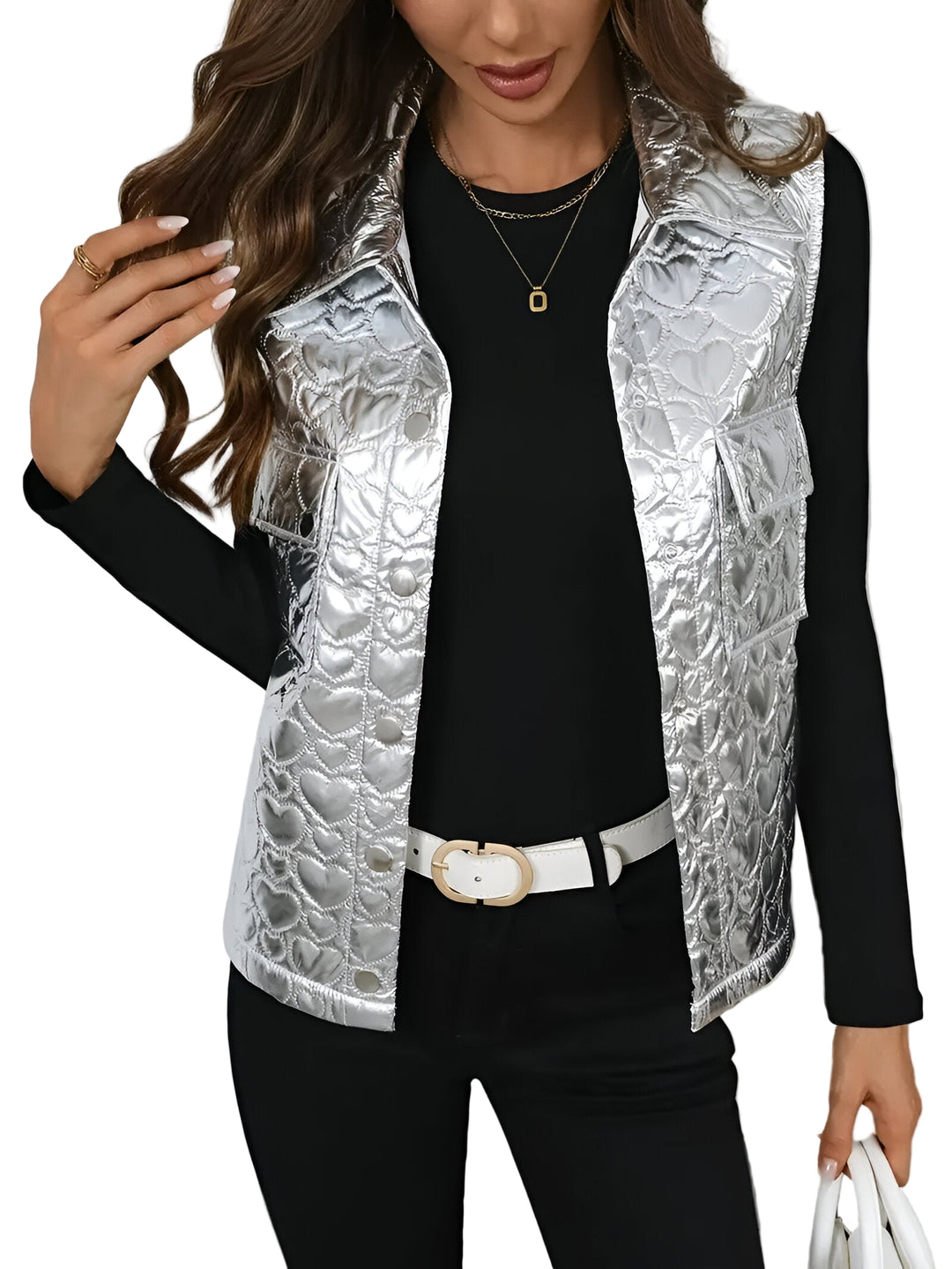 Femme portant un gilet sans manches argenté au fini métallisé avec un motif matelassé en forme de cœur. Elle le combine avec un haut noir à manches longues, un pantalon assorti et des accessoires dorés. Une ceinture blanche et un sac clair complètent son look moderne et chic.