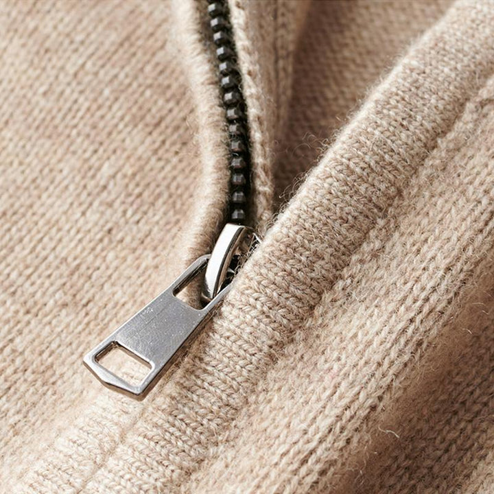 Gros plan sur la fermeture éclair métallique d’un pull en maille beige, montrant le col zippé et la finition tricotée.