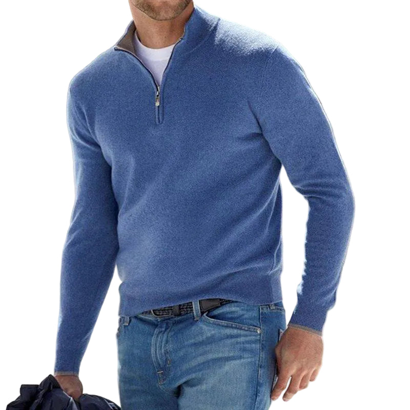 Pull pour homme bleu avec col montant et fermeture zippée courte, coupe ajustée à manches longues, porté avec un jean bleu dans un décor extérieur.