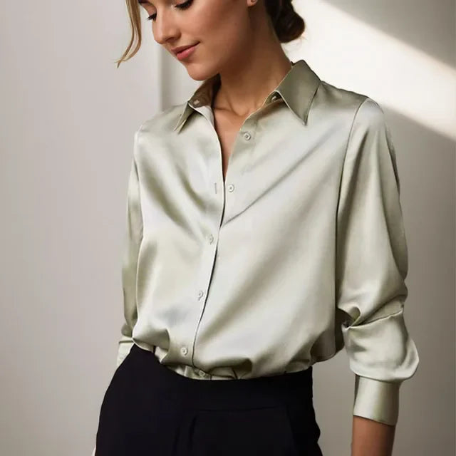 Chemisier en satin vert clair pour femme, avec un col classique et des boutons sur le devant. Le vêtement présente une coupe ample, des manches longues légèrement retroussées aux poignets, et est porté avec un pantalon noir élégant. Idéal pour une allure sophistiquée, parfaite pour le bureau ou une soirée raffinée.