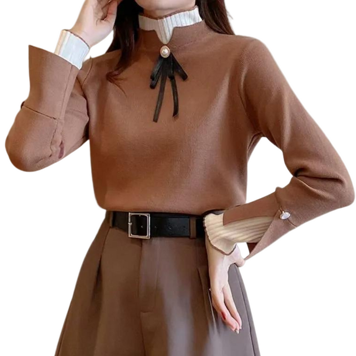Femme portant un pull brun à manches longues avec un col montant blanc côtelé. Le col est orné d’un ruban noir noué sous un bouton doré, ajoutant une touche raffinée. Les poignets présentent également des détails blancs contrastants et des boutons décoratifs. Le vêtement est associé à un pantalon taille haute assorti et une ceinture noire, créant un look élégant et moderne parfait pour l’hiver.