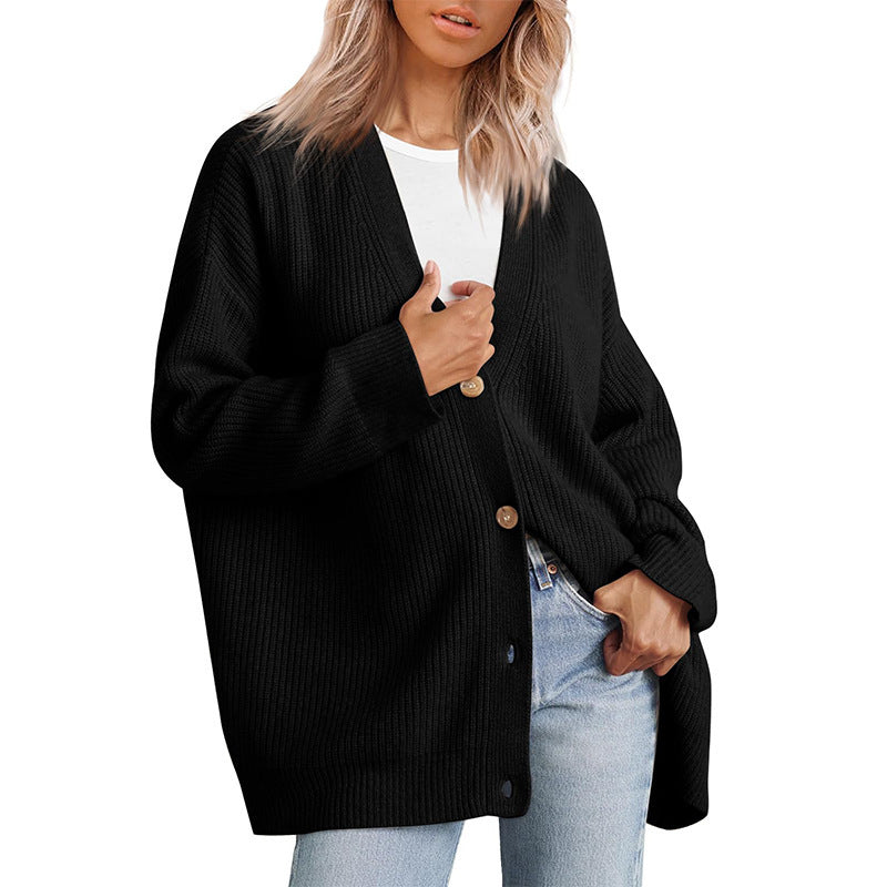 Femme portant un cardigan oversize noir à col en V, fermé par de gros boutons, superposé à un t-shirt blanc et assorti à un jean clair.