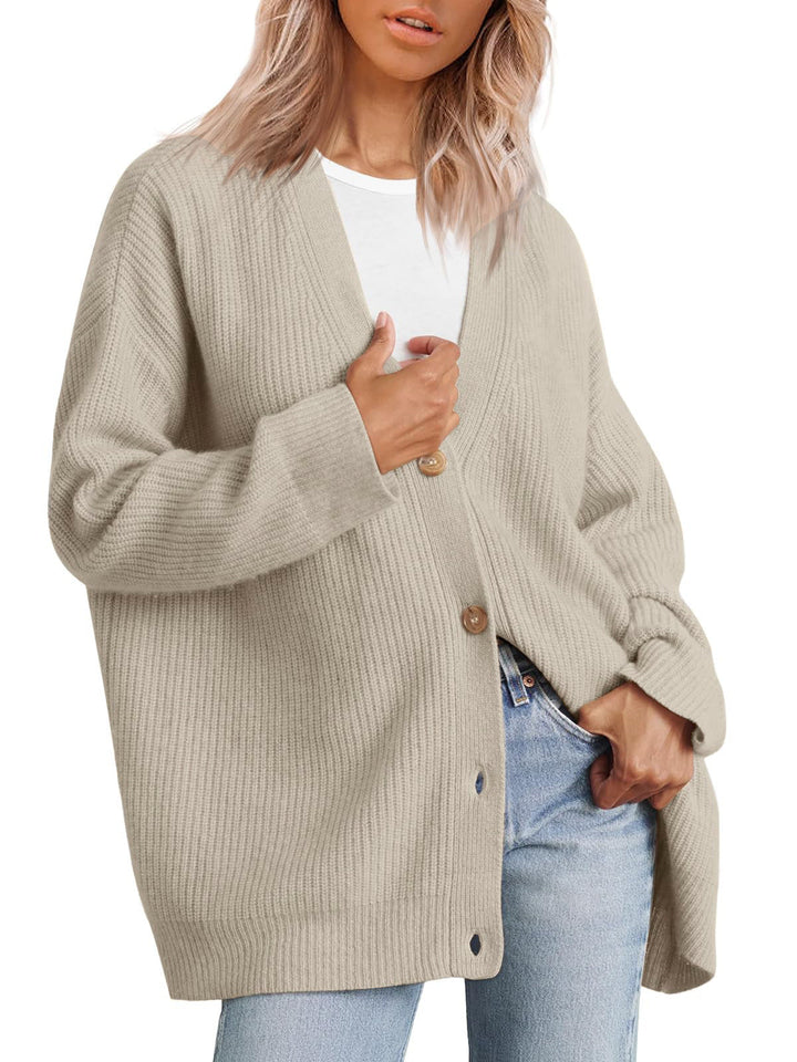 Femme portant un cardigan oversize beige clair à col en V, fermé par de gros boutons, superposé à un t-shirt blanc et assorti à un jean clair.