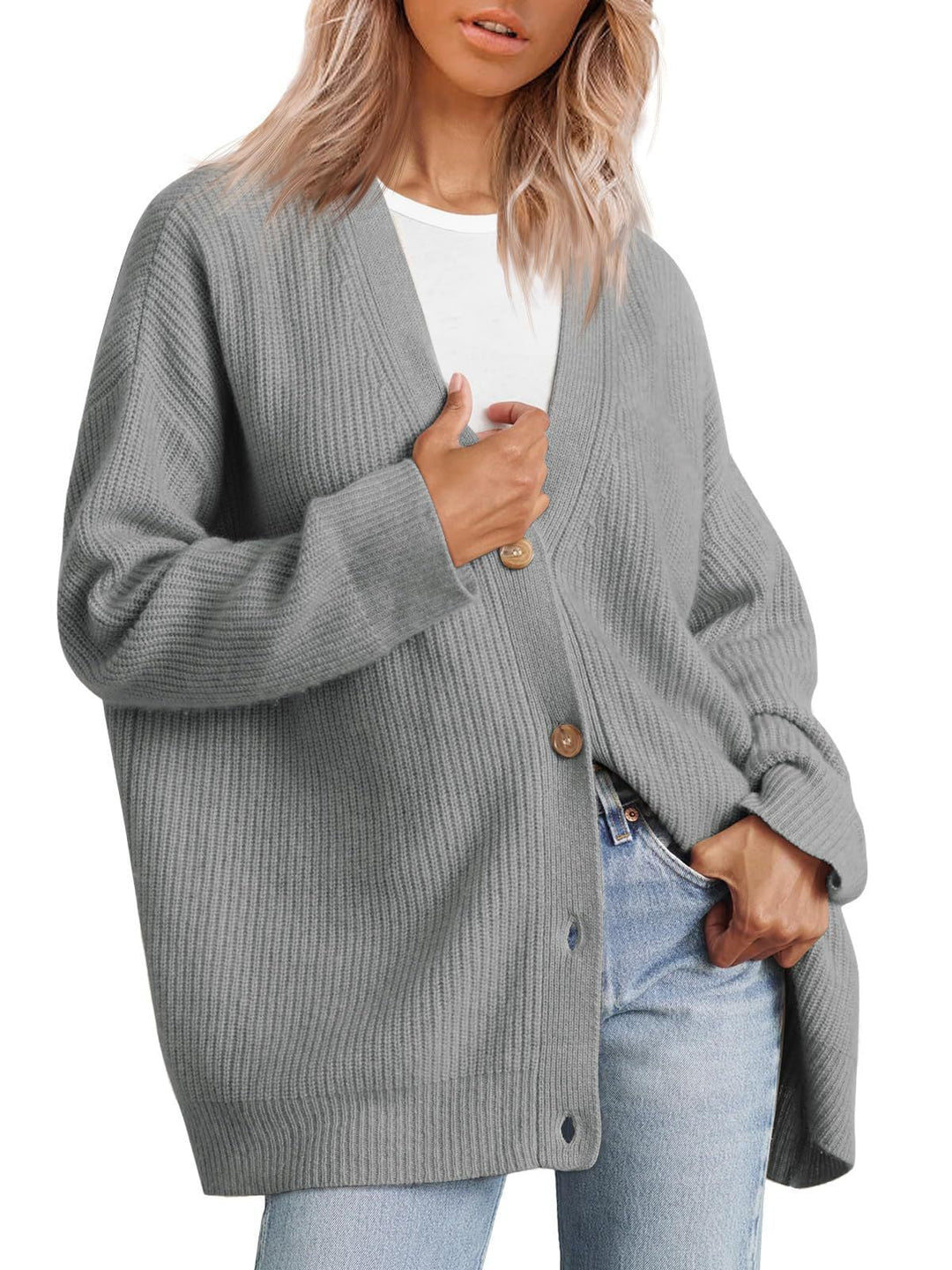 Femme portant un cardigan oversize gris à col en V, fermé par de gros boutons, superposé à un t-shirt blanc et assorti à un jean clair.
