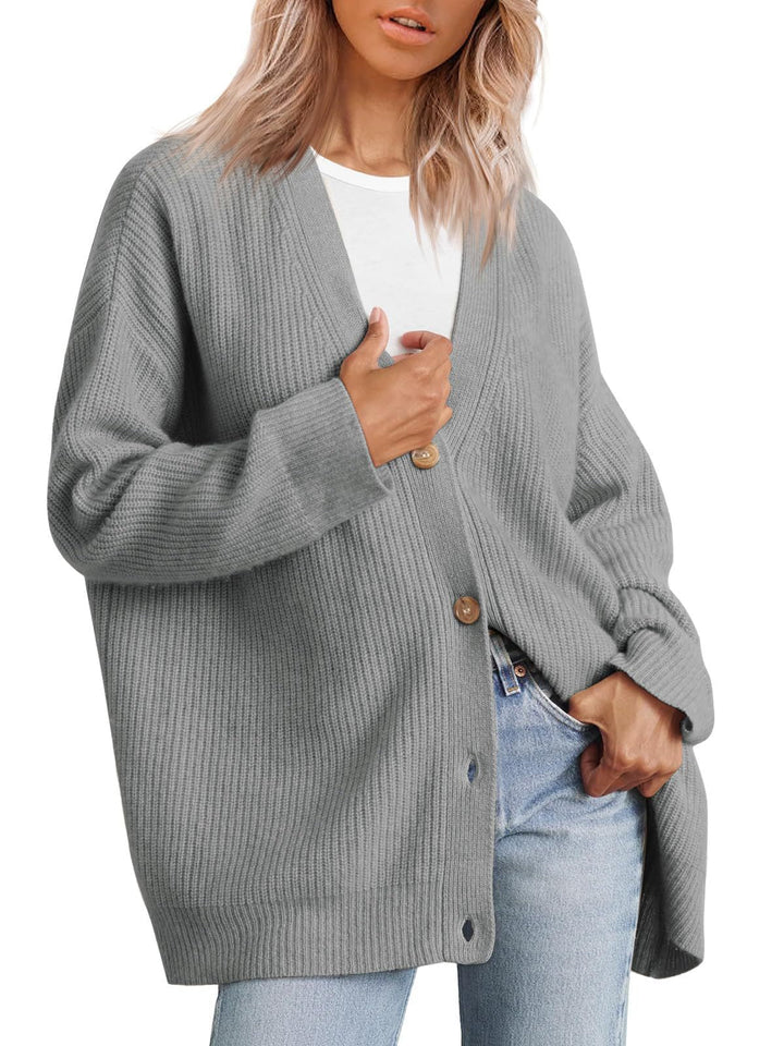 Femme portant un cardigan oversize gris à col en V, fermé par de gros boutons, superposé à un t-shirt blanc et assorti à un jean clair.