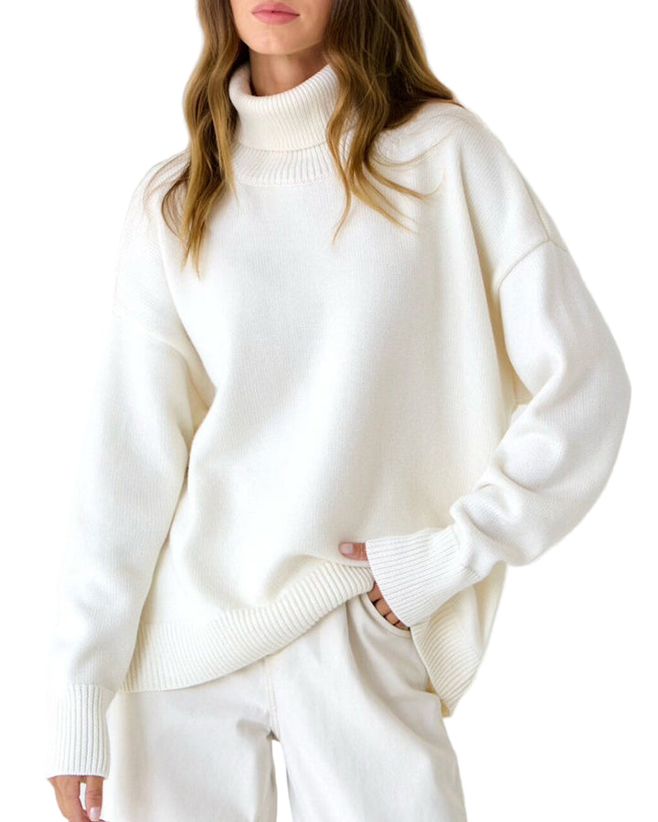 Femme portant un pull à col roulé blanc à la coupe ample et minimaliste. Le tricot présente des finitions côtelées aux poignets, au col et à la base, ajoutant une touche de texture élégante. L’ensemble monochrome, assorti à un pantalon clair, crée un look épuré et moderne idéal pour un style hivernal chic et confortable.