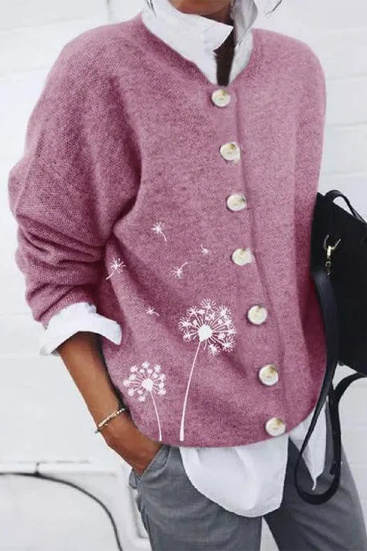 Cardigan pour femme de couleur rose, orné de gros boutons nacrés et d’un motif délicat de pissenlits blancs, porté avec une chemise blanche pour un style moderne et décontracté.