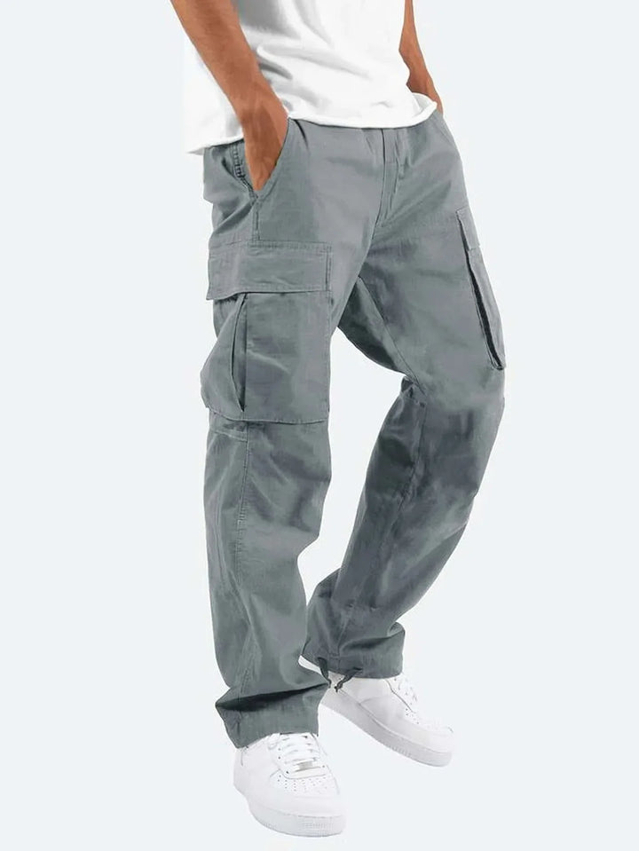 Homme portant le pantalon droit Aymeric pour hommes, style cargo gris avec poches latérales pratiques, coupe droite confortable et bas ajustables, associé à un t-shirt blanc et des baskets blanches  look tendance et urbain.