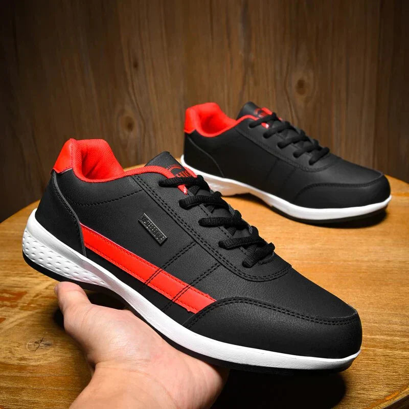 Paire de chaussures décontractées Benoît pour homme en noir avec détails rouges, lacets noirs et semelle blanche amortissante, présentées sur une table en bois, look moderne et confortable.