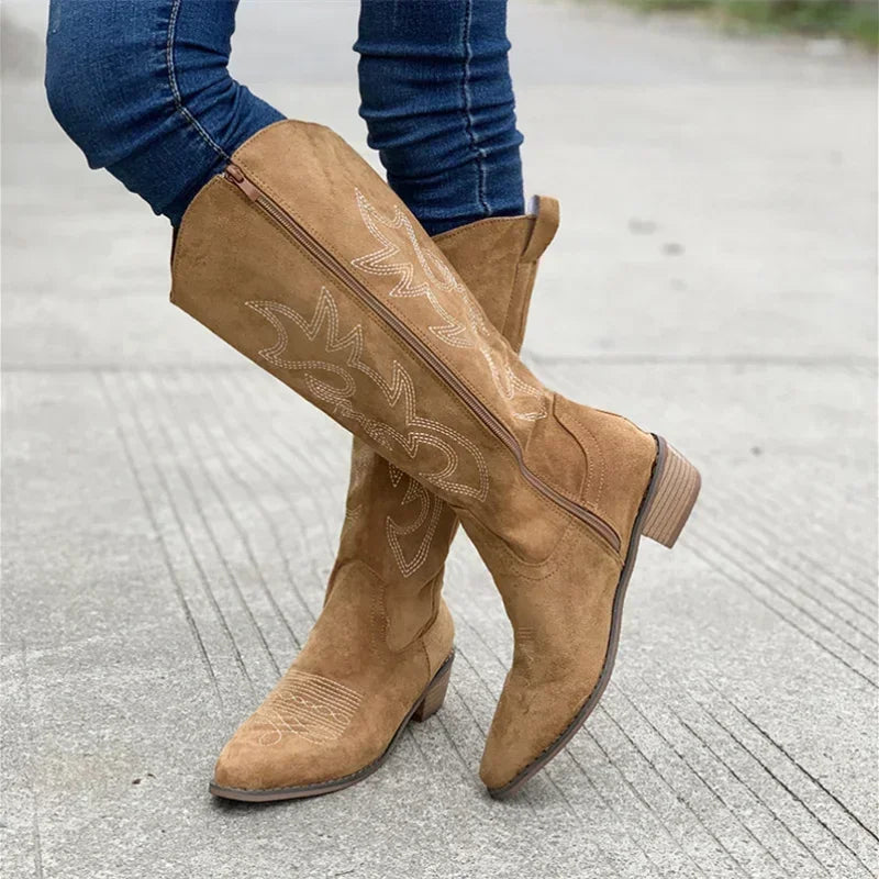 Bottes de cowboy en suède beige pour femme, avec des broderies décoratives sur la tige. Elles présentent une fermeture éclair latérale, un talon en bois et une forme pointue à l'avant, offrant un style chic et moderne.